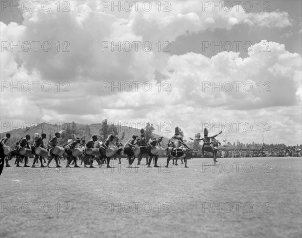 A line of Wakamba dancers. An audience watches as a long line of Wakamba men perform a dance with drums for Princess Margaret's visit. Machakos, Kenya, 22 October 1956. Machakos, East (Kenya), Kenya, Eastern Africa, Africa.