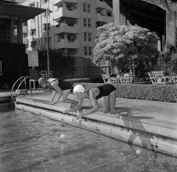 Olympic swimmers dive in. Two female swimmers competing in the 1956 Olympic Games are captured mid-dive as they plunge into a swimming pool at the start of a practice race. Kenya, 2 November 1956. Kenya, Eastern Africa, Africa.