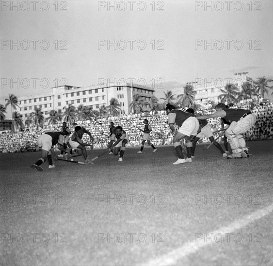 Pre-Olympic hockey match. A pre-Olympic hockey match between national teams from Kenya and Goa. Three players attempt to win the ball whilst defenders and the goal keeper watch on. Kenya, 2 November1956. Kenya, Eastern Africa, Africa.