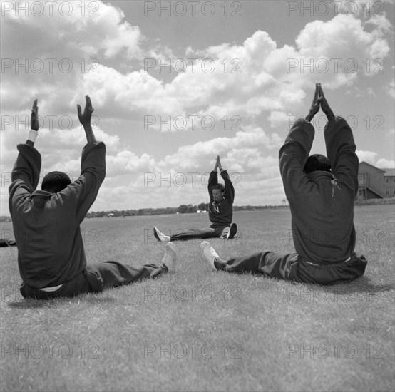 Olympic training under Archie Evans. Athletes in the Kenyan Olympic team stretch their arms in the air at a pre-Olympic training session run by Archie Evans. Australia, 5 November 1956., Australia, Oceania.