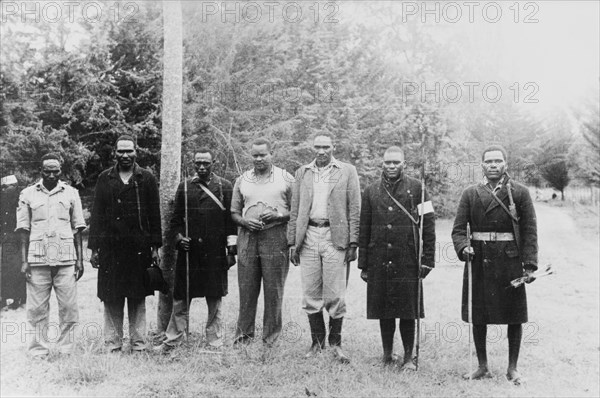 A farmer's Home Guard. Members of a European settler's Home Guard pose for the camera holding spears and bows and arrows. Some wear military great coats, possibly a leftover from service in the King's African Rifles during the Second World War. Kenya, circa 1952. Kenya, Eastern Africa, Africa.