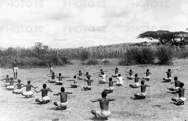 Kikuyu children exercising. Children perform coordinated exercises in a secure village established for the families of the Kikuyu Home Guard. Kenya, circa 1953. Kenya, Eastern Africa, Africa.