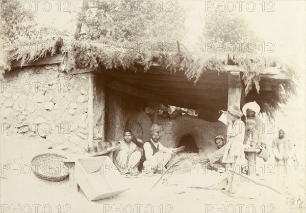 An Indian bakery. A group of Indian men and boys sit around a clay oven at a baker's shop, waiting for a fresh batch of bread to bake. India, circa 1895. India, Southern Asia, Asia.