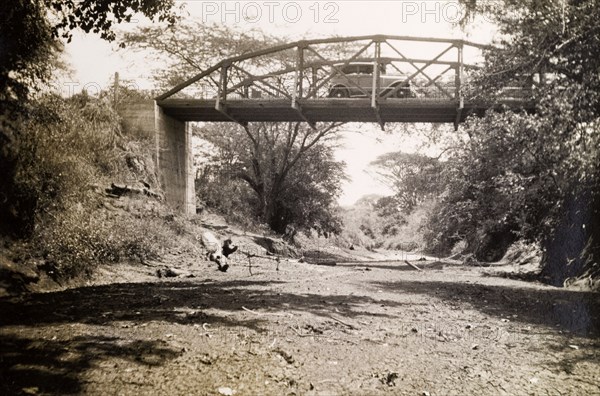 Hal Wallhouse's bridge. A motorcar drives across a small bridge that spans a dried up watercourse. The original caption identifies this as 'Hal's bridge, shipped from Liverpool'. Probably Tanganyika Territory (Tanzania), circa 1935. Tanzania, Eastern Africa, Africa.