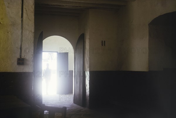 Interior of slave market, Elmina Castle. A sunlit doorway leads into the dark interior of the old slave market at Elmina Castle. An original caption tells us that 'slaves were viewed by buyers through squint holes' in this room. Ghana, circa 1965. Elmina, Central (Ghana), Ghana, Western Africa, Africa.