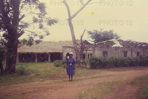 Matron Ifeka at Iyi Enu. A nurse in uniform identified as 'Matron Ifeka' stands outside the Iyi Enu Church of Nigeria Hospital. The buildings behind her are covered with bullet holes, damaged in raids carried out during the Nigerian Civil War (1967-70). Iyi Enu, Nigeria, May 1970. Iyi Enu, Anambra, Nigeria, Western Africa, Africa.