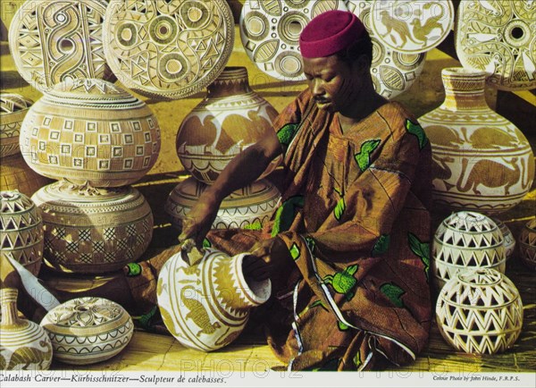 Carving calabashes, Nigeria. A colourful tourist postcard depicts a Nigerian craftsman at work, sitting cross-legged on the ground as he carves decorative patterns onto dried calabashes or gourds. A selection of finished gourds are lined up on display behind him. Nigeria, circa 1975. Nigeria, Western Africa, Africa.