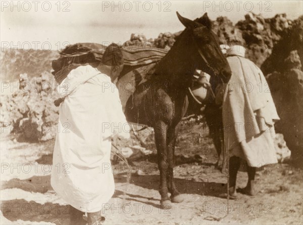 Loading up a mule, Morocco. Two Moroccan men load up their mule with blankets and baskets at a rocky outcrop in the desert. Morocco, 1898. Morocco, Northern Africa, Africa.