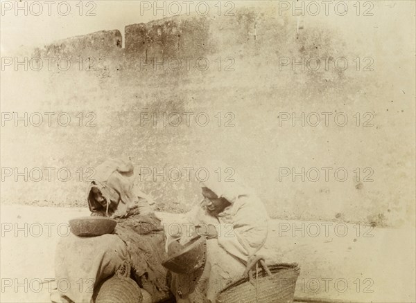 Moroccan beggars. Moroccan beggars dressed in ragged robes, sit on the street, begging bowls and baskets in hand. Morocco, 1898. Morocco, Northern Africa, Africa.