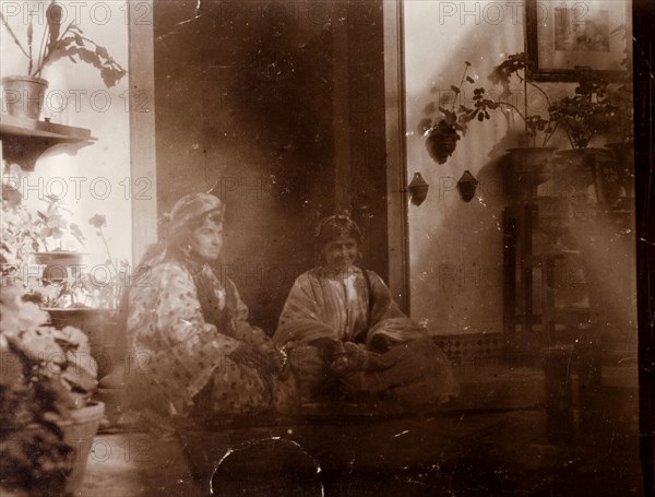 Mrs Russi dressed as a 'moorish woman'. Mrs Russi, a European woman, sits in the doorway of a colonial house dressed up as a 'moorish woman'. Clothed in a robe, she wears her hair (or wig) long and loose and is accompanied by a Moroccan girl whio sits cross-legged by her side. Safi, Morocco, 1898. Safi, Safi, Morocco, Northern Africa, Africa.