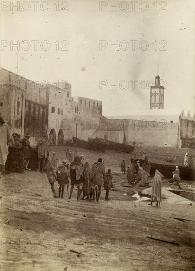 Harbourside market place, Safi. Morrocan people mill about at a market place near the harbour in Safi. Fishing boats can be seen moored on the harbourside. Safi, Morocco, 1898. Safi, Safi, Morocco, Northern Africa, Africa.