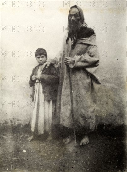 Jewish beggar, Safi. A barefoot Jewish beggar of gaunt appearance rests his hand on a young boy's shoulder. Safi, Morroco, 1898. Safi, Safi, Morocco, Northern Africa, Africa.