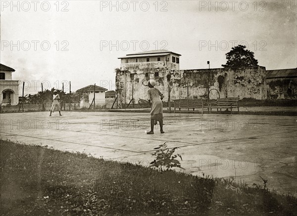 Kenyan servants playing tennis. Two African boys play tennis on a court begind Fort Jesus, part of the grounds of the Mombasa Sports Club. Mombasa, British East Africa (Kenya), 1906. Mombasa, Coast, Kenya, Eastern Africa, Africa.