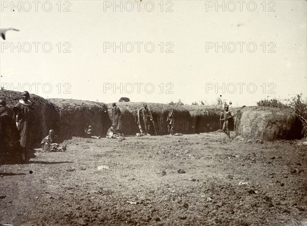 Outside a Maasai village. A group of Maasai are pictured outside the protective mud wall of their village. British East Africa (Kenya), 1906. Kenya, Eastern Africa, Africa.