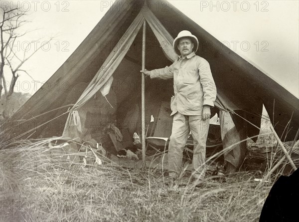 Frederick Stanbury outside a tent. Frederick Stanbury poses for the camera in front of a small, open tent near Lake Baringo. British East Africa (Kenya), 1906., Rift Valley, Kenya, Eastern Africa, Africa.