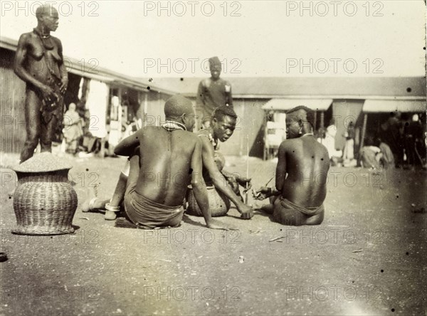 Luo men and women at Kisumu market. Luo men and women chat, seated on the ground outside a local market. Kisumu, British East Africa (Kenya), 1906. Kisumu, Nyanza, Kenya, Eastern Africa, Africa.