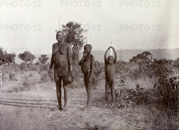 Luo woman and children carrying milk. A Luo women and her two children balance tall bottles of milk on the heads. Kavirondo, British East Africa (Kenya), 1906. Kavirondo, Nyanza, Kenya, Eastern Africa, Africa.