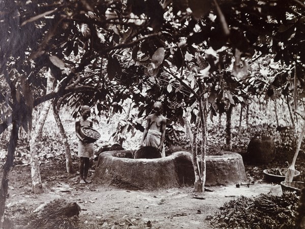 Female palm oil workers. Two women crushing palm oil nuts in a mud enclosure. Probably Badagry, Nigeria, circa 1925. Nigeria, Western Africa, Africa.