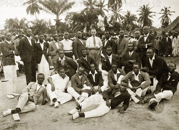 H. Montmorency at Empire Day celebrations. District Officer H. Montmorency (the European man in the centre) attends Empire Day celebrations with his Nigerian assistants or students. The young Nigerian men surrounding him wear smart Western-style clothing. Badagry, Nigeria, May 1924. Badagry, Lagos, Nigeria, Western Africa, Africa.