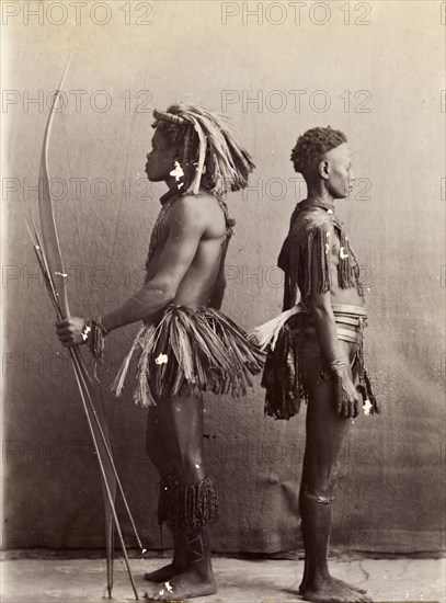 Andaman Islanders. A man and a woman from the Andaman Islands stand, back to back in profile, against an unpainted backdrop. The man holds a bow and long arrows: both wear grass-like aprons and neckpieces. Andaman Islands, India, circa 1900., Andaman and Nicobar Islands, India, Southern Asia, Asia.