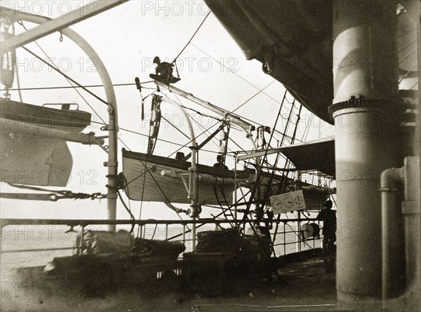 Lifeboats on RIMS 'Investigator'. A crew member perches precariously above a lifeboat on board RIMS 'Investigator'. Originally captioned 'sounding lead', he may be extending the ship's sounding line, a nautical plumb line for determining the depth of water. Indian Ocean, circa 1900., Southern Asia, Asia.