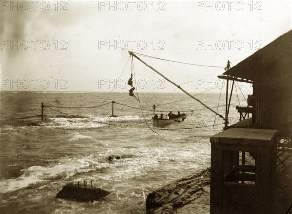 Arriving at Alguada Reef. A small boat arrives in the dock at Alguada Reef lighthouse, ferrying crew members from a Royal Indian Marine Service ship to dry land. Burma (Myanmar), circa 1900. Burma (Myanmar), South East Asia, Asia.