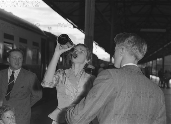 Wendy Winter drinks champagne. Wendy Winter (nee Allen) drinks champagne from the bottle before departing on a train with her newlywed husband, Dudley Winter. Kenya, 30 December 1952. Kenya, Eastern Africa, Africa.