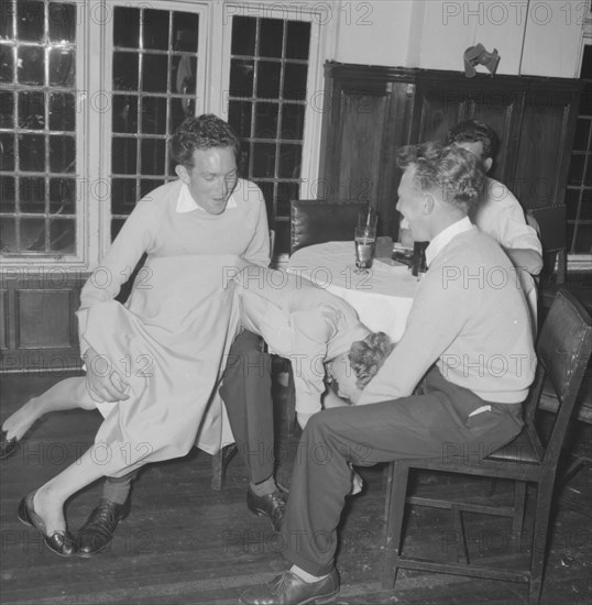 Jazz Ball antics. Three young men in casual dress joke together over the apparently accidental manouevre of a young woman who has fallen across one of their laps at a Jazz Ball. She shares the joke. Kenya, 21 September 1957. Kenya, Eastern Africa, Africa.