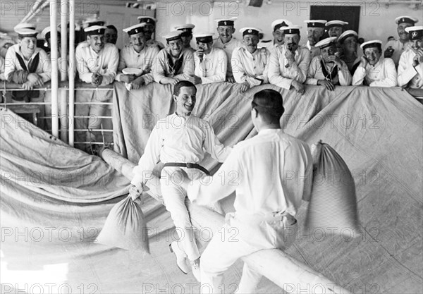 Pillow fight aboard HMS Medina. Captain Bryan Godfrey-Faussett, Equerry to King George V, and the Fleet Surgeon, stage a pillow fight on a greased spar aboard HMS Medina. The royal yacht was transporting King George V and Queen Mary to India for the Coronation Durbar at Delhi. Indian Ocean near Mumbai, India, circa 30 November 1911. India, Southern Asia, Asia.