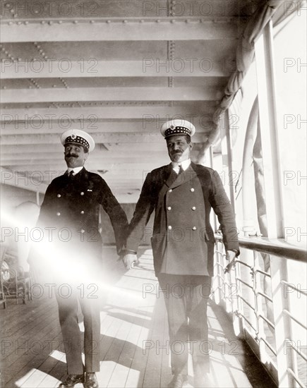 Officers aboard the S.S. Balmoral Castle. Two British naval officers hold hands and pull faces for the camera as they pose on the deck of the S.S. Balmoral Castle. The ship was transporting the Duke and Duchess of Connaught to South Africa, where they were due to open the new Union Parliament in Cape Town. Probably Atlantic Ocean, Africa, October 1910. Africa.