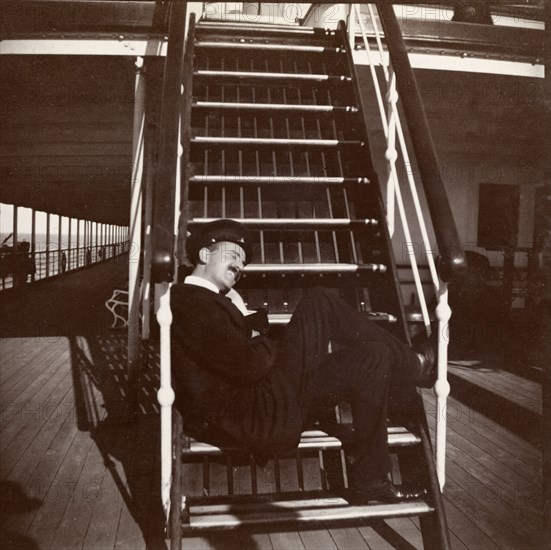 Seating arrangements on the S.S. Balmoral Castle. A passenger aboard the S.S. Balmoral Castle sits on steps leading to the upper deck. The ship was transporting the Duke and Duchess of Connaught to England from South Africa, where they had recently opened the new Union Parliament in Cape Town. Probably Indian Ocean, Africa, circa 2 December 1910. Africa.