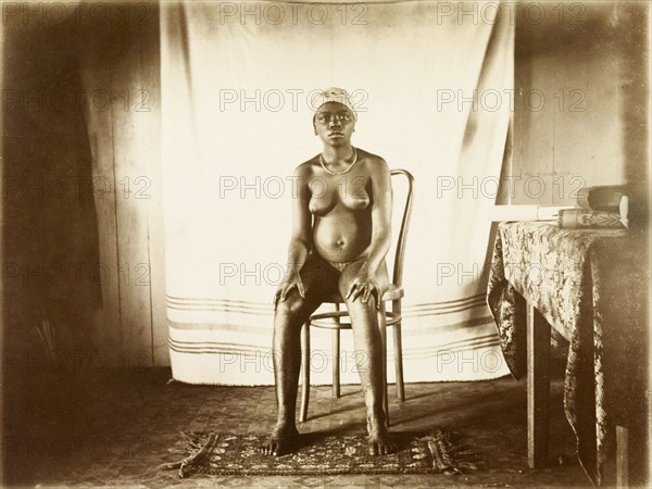 Young woman from Bioko. Portrait of a young woman from Bioko. Posed seated against a makeshift backdrop, she is nearly naked and displays scarification marks on her belly. Bioko, Equatorial Guinea, circa 1930., Bioko Norte, Equatorial Guinea, Central Africa, Africa.