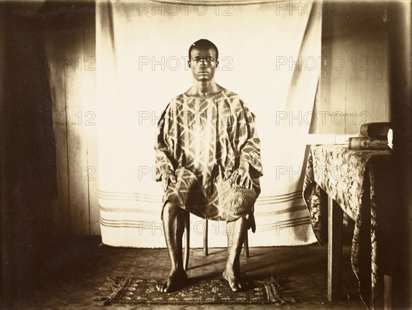 Young man from Bioko. Portrait of a traditionally dressed young man from Bioko, posed seated against a makeshift backdrop. Bioko, Equatorial Guinea, circa 1930., Bioko Norte, Equatorial Guinea, Central Africa, Africa.