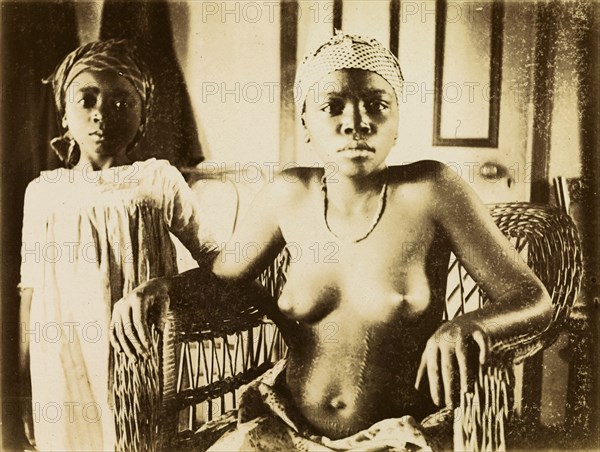 Inhabitants of Bioko. Portrait of a girl and a young woman from Bioko. Posed seated in a wickerwork chair, the semi-naked woman displays scarification marks on her belly. Bioko, Equatorial Guinea, circa 1930., Bioko Norte, Equatorial Guinea, Central Africa, Africa.