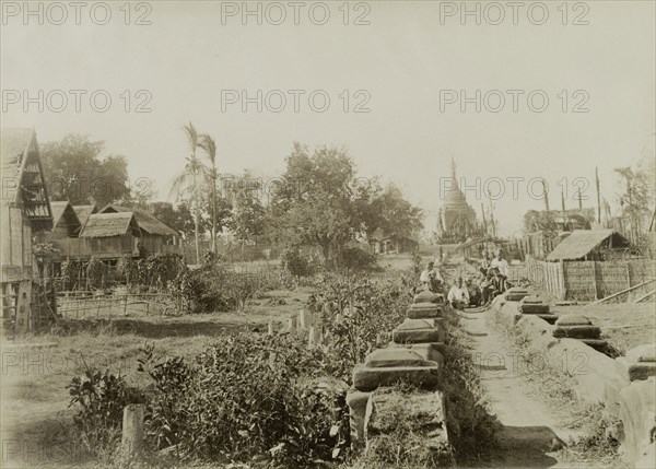 Wuntho after its capture. A pathway flanked by low walls leads past a number of thatched dwellings towards the 'Pon-gyi kyaung' (Buddhist monastery) at Wuntho. This scene was captured shortly after British forces took control of the town following a conflict with Burmese rebels. Wuntho, Burma (Myanmar), 1891. Wuntho, Sagaing, Burma (Myanmar), South East Asia, Asia.