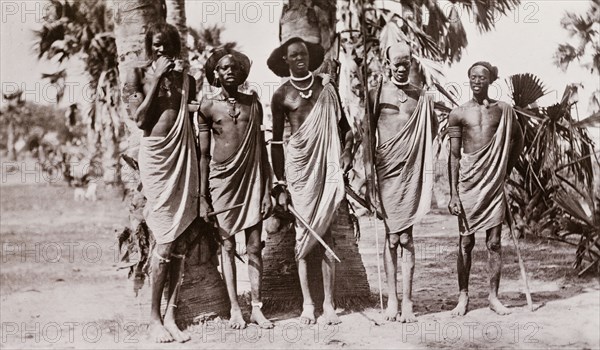 Portrait of five Shilluk warriors. Five Shilluk warriors pose for a group portrait. The men have distinctive hairstyles and stand in a row carrying spears. Upper Nile State, Sudan, circa 1910., Upper Nile, Sudan, Eastern Africa, Africa.