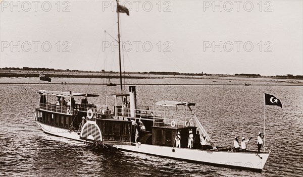 Paddle steamer on the River Nile. A paddle steamer named 'The Elfin' travels along the River Nile, flying a British Empire flag at its stern and a Ottoman Empire flag at its bow. Near Sudan, circa 1910. Sudan, Eastern Africa, Africa.