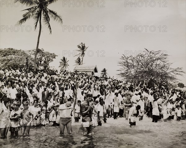 Tanzania bids farewell to Sir Richard Turnball. A racially mixed crowd, comprising both Africans and Europeans, gathers on a beach to wave farewell to Sir Richard Turnbull (1909-1998), the last British colonial Governor of Tanganyika, as he leaves the country aboard HMS Loch Ruthven. Tanganyika (Tanzania), 8 December 1962. Tanzania, Eastern Africa, Africa.