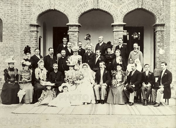 A British wedding in India, 1899. A newly-wed British couple pose for a group portrait with their wedding guests, all of whom wear formal attire in typical Victorian style. An Indian ayah (nursemaid), holding a British baby, stands in front of a gentleman identified as the British author and journalist, Louis Tracy. Porbably India, 2 January 1899. India, Southern Asia, Asia.