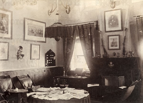 Ante room in a British Army mess building. Interior shot of an ante room in a British Army mess building, used by off-duty soldiers as a place to relax and socialise. Framed pictures and mounted antelope skulls adorn the walls, whilst padded chairs surround a table sprawling with papers. Chaman, Baluchistan, India (Balochistan, Pakistan), 1905. Chaman, Balochistan, Pakistan, Southern Asia, Asia.