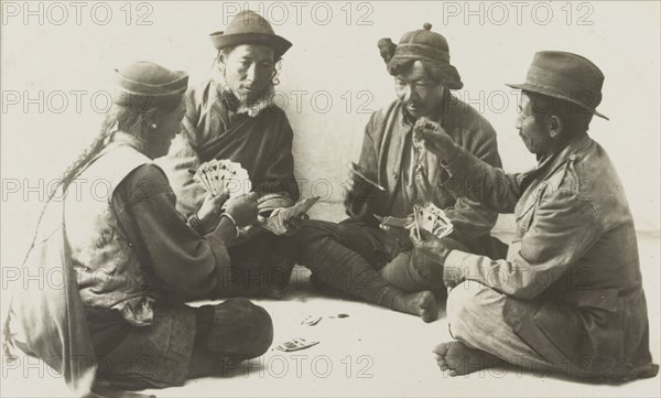 Rickshaw drivers enjoy a game of cards. Four rickshaw drivers sit cross-legged in a circle on the ground, each holding a hand of fanned-out playing cards during a game of cards. Probably Nepal, circa 1922. Nepal, Southern Asia, Asia.