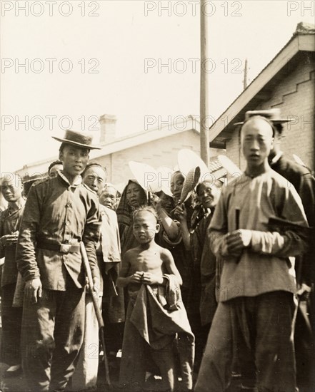 At a station on the Peking to Hankow railway line. A crowd of people gaze curiously into the camera at a railway station on the Peking (Beijing) to Hankow (Hankou) railway line. The man in uniform on the left is possibly a station official. Eastern China, circa 1910. China, People's Republic of, Eastern Asia, Asia.