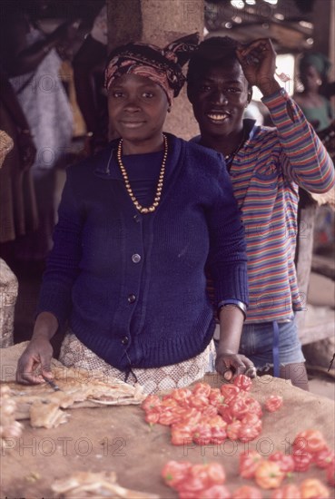 Preparing food at Bakau market. An African man and woman smile for the camera as they prepare food on a stall at Bakau market. Bakau, Gambia, circa 1985. Bakau, West (Gambia), Gambia, Western Africa, Africa.