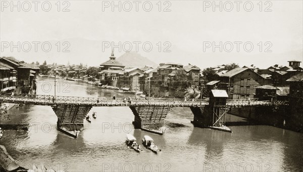 The Jhelum River at Srinagar. Several shikaras pass beneath a wooden road bridge spanning the Jhelum River at Srinagar. Srinagar, Jammu and Kashmir State, India, circa 1927. Srinagar, Jammu and Kashmir, India, Southern Asia, Asia.