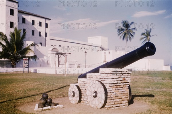 A cannon at Elmina Castle. A cannon and a heap of cannon balls are positioned as a monument in front of Elmina Castle. Elmina, Ghana, circa 1959. Elmina, Central (Ghana), Ghana, Western Africa, Africa.