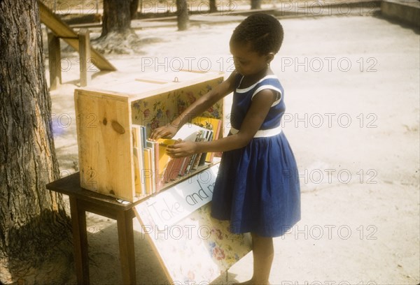 Browsing books in a class library. A young girl browses through books in the class library at Philip Quaque Girls School. Cape Coast, Ghana, March 1958. Cape Coast, Central (Ghana), Ghana, Western Africa, Africa.