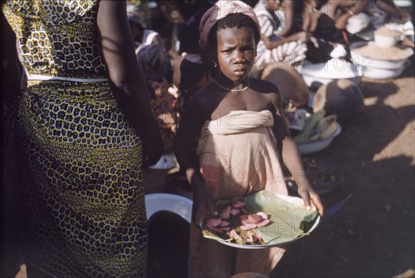 Kola nut seller. A young girl sells kola nuts from a leaf-lined plate at Tamale market. Tamale, Ghana, circa 1961. Tamale, North (Ghana), Ghana, Western Africa, Africa.