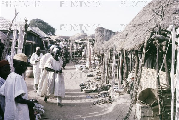 A marketplace in Kano. Stalls with thatched canopies shelter goods from the sun in a busy marketplace in Kano. Kano, Nigeria, October 1963. Kano, Kano, Nigeria, Western Africa, Africa.