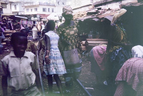 Old railway track running through Freetown market. Shoppers walk along a disused railway track running through the centre of a busy marketplace. Freetown, Sierra Leone, 13 February 1964. Freetown, West (Sierra Leone), Sierra Leone, Western Africa, Africa.