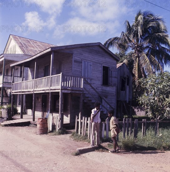 Wooden house in Belize. Two boys chat on a street corner outside a wooden, two-storey house in Danriga, which features a veranda and balcony. Danriga, Belize, circa 1975. Dangriga, Stann Creek, Belize, Central America, North America .